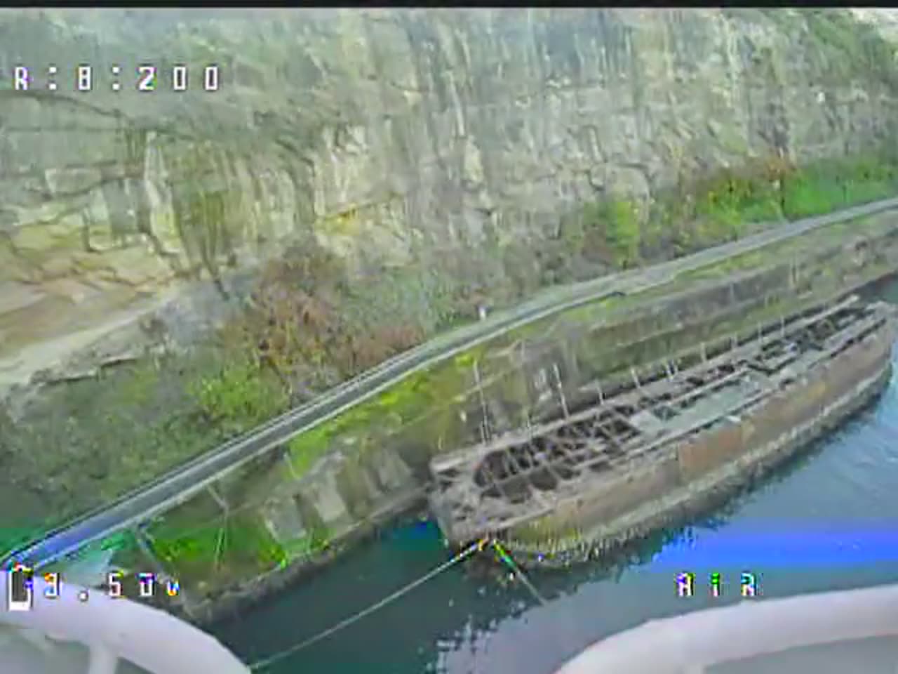 A frame from the drone's DVR, flying low over water beside a sandstone cutting with a derelict barge in the shot